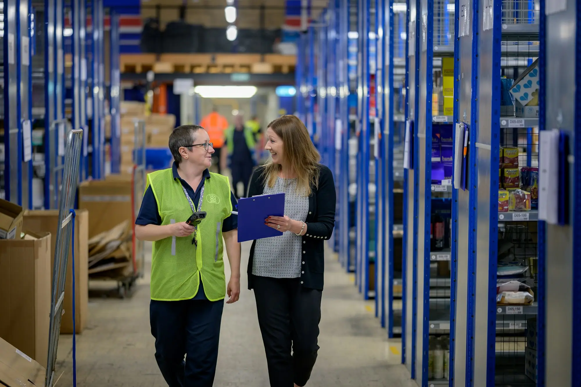 Warehouse owner and staff member checking stock in a busy aisle